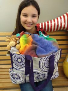 Christin Love sits on the bench in our front lobby holding one of the totes that is given to families checking into the House. The bag includes one of the blankets made by the class at a North Carolina school.