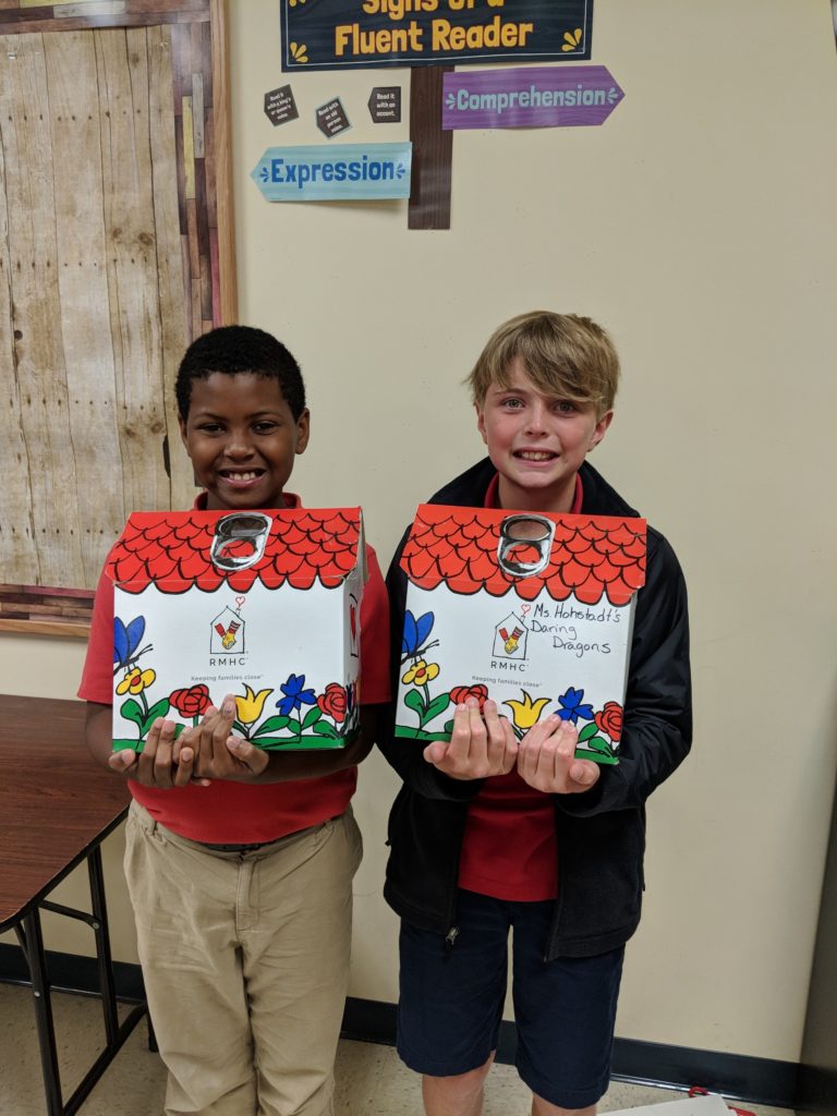 Two boys hold boxes shaped like houses which hold donated pop-tabs.
