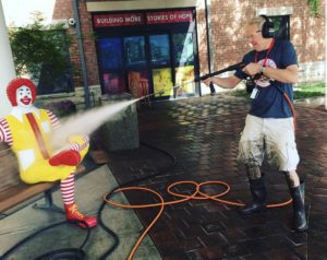 Volunteer is using a power washer on the Ronald McDonald sculpture outside our front doors.
