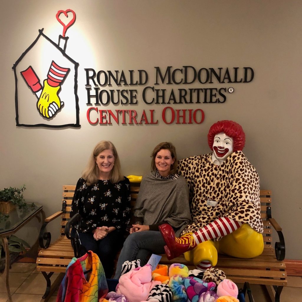 Two women sit on the lobby bench next to our Ronald McDonald statue displaying donated ponchos.