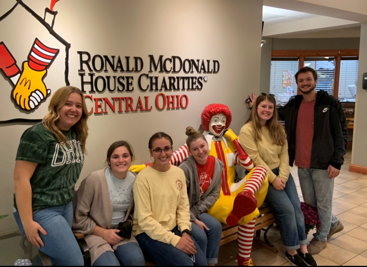 Six students pose with Ronald McDonald bench statue in our front lobby.