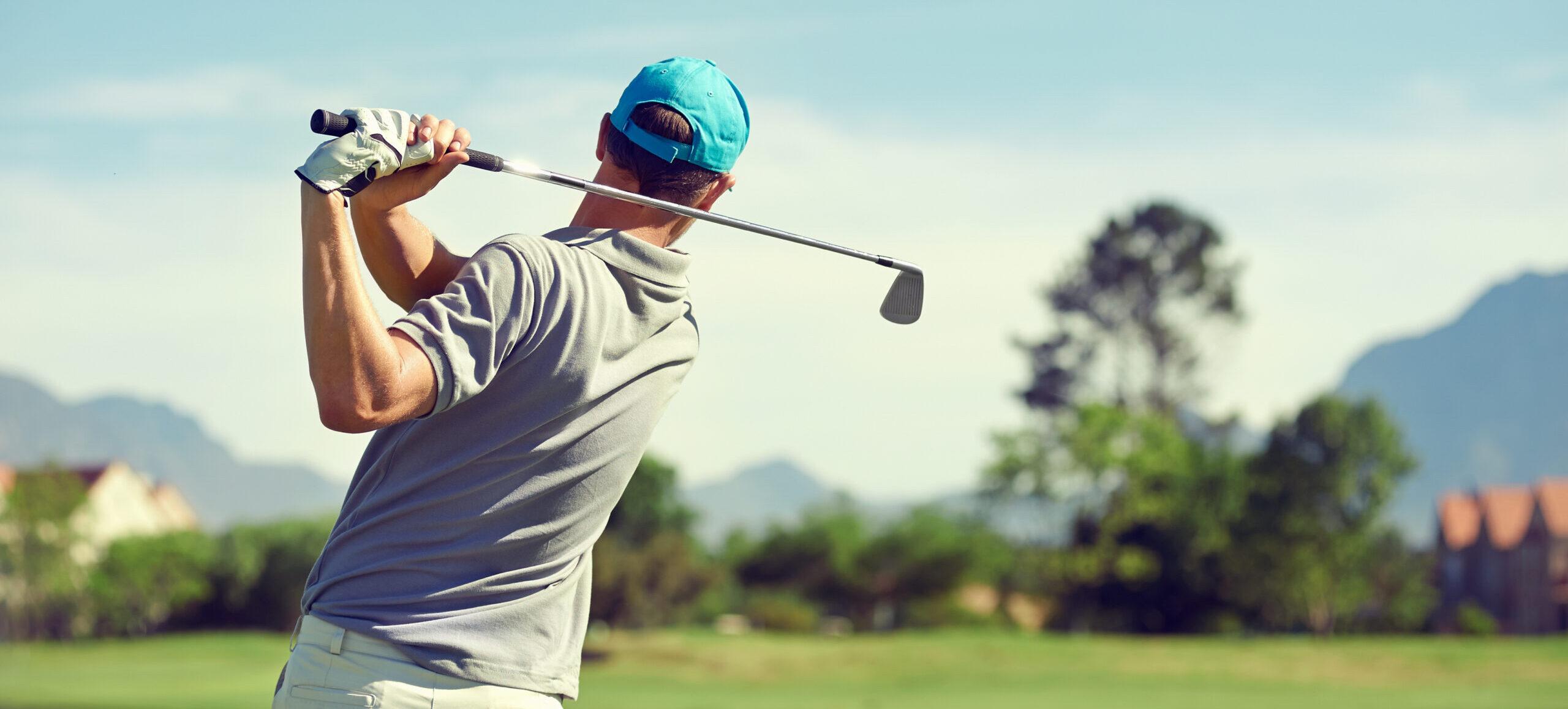 man in light blue cap swinging golf club