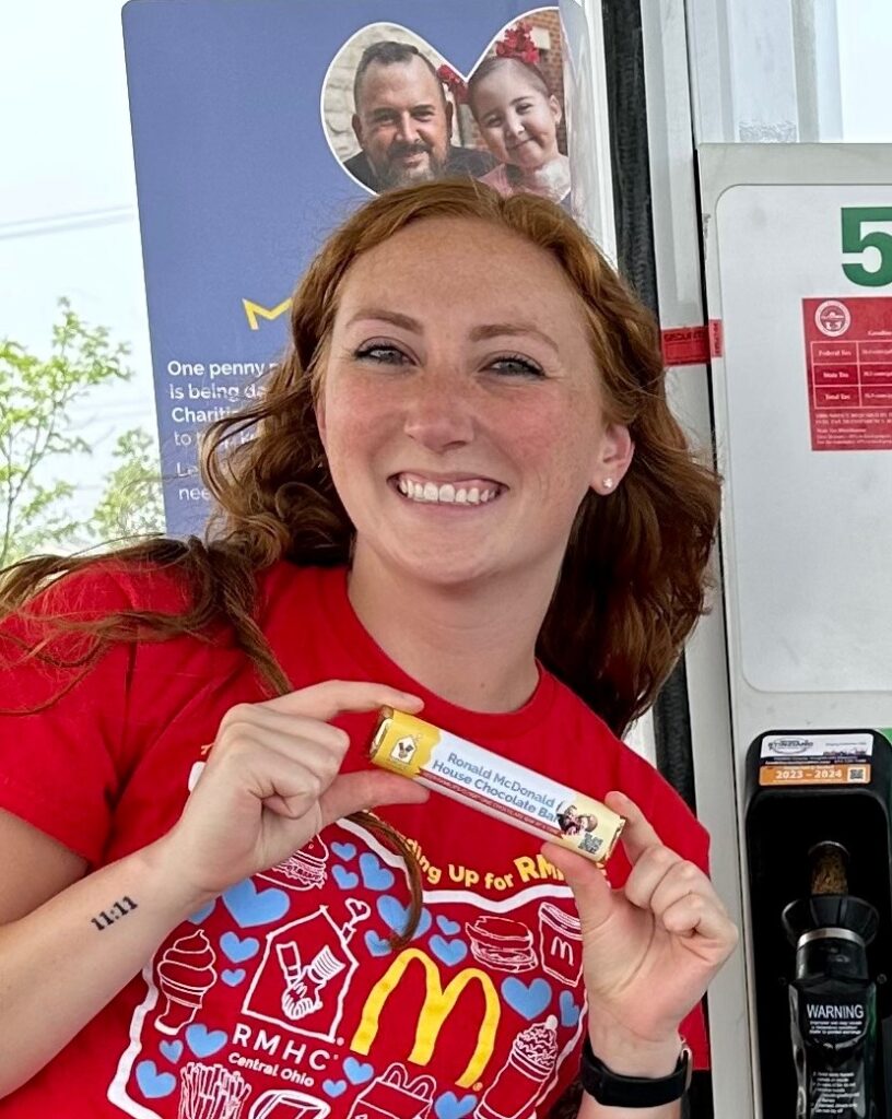 A smiling person hold the RMHC-branded chocolate bar at a newly RMHC-branded gas pump.