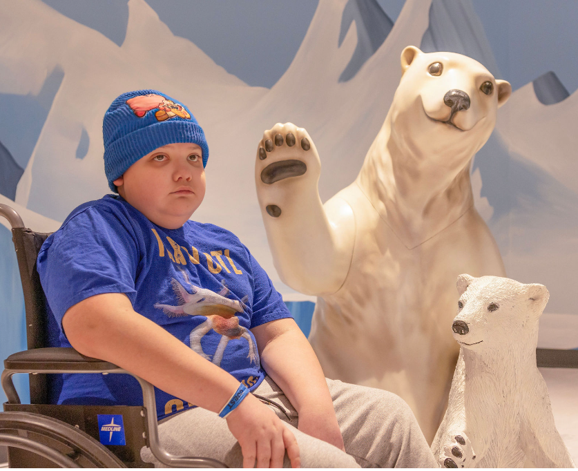 Boy in wheelchair sits next to statues of polar bears.