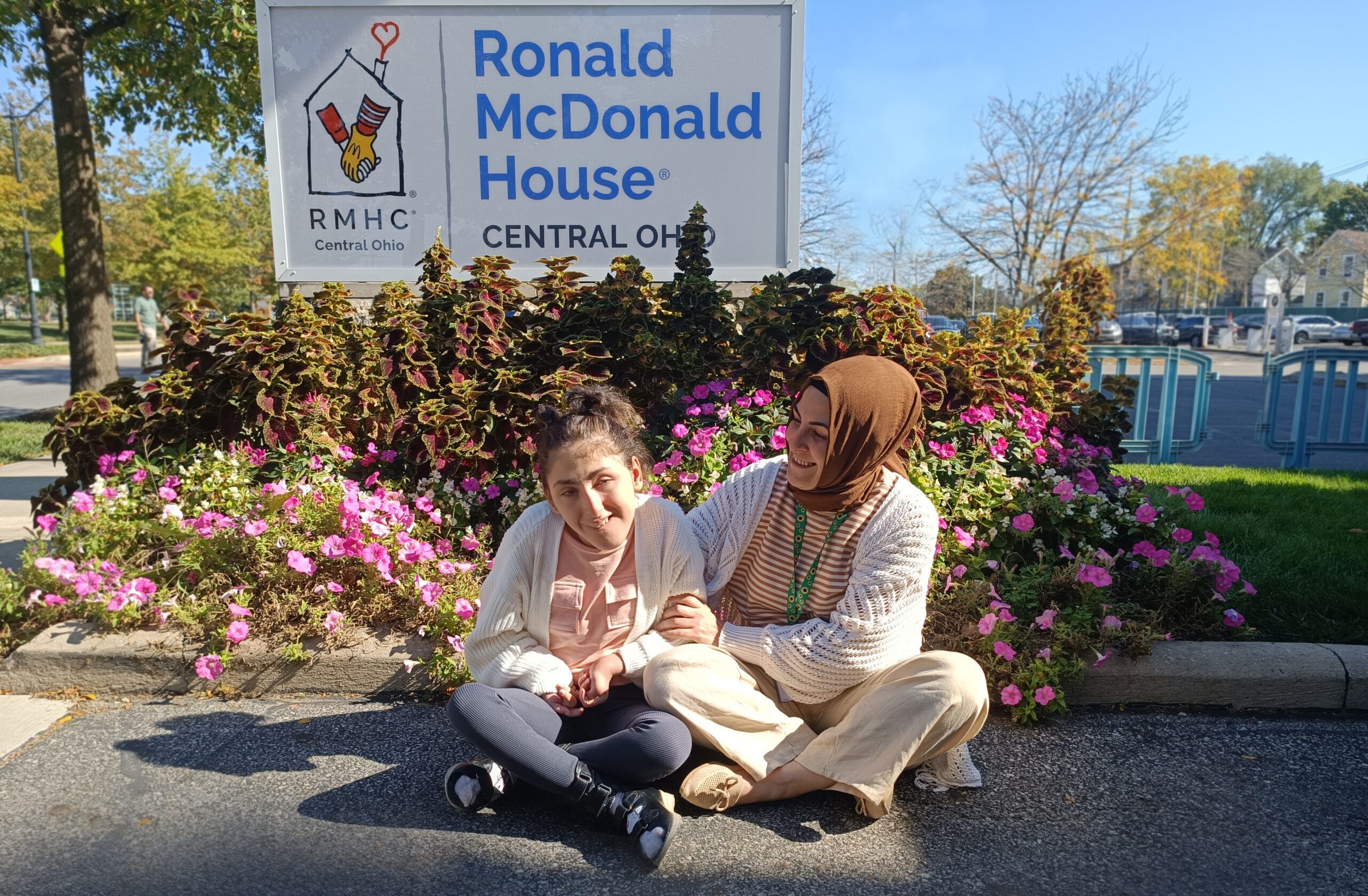 A mother and daughter sit on the curb in front of the Ronald McDonald House sign outside the House in Columbus.